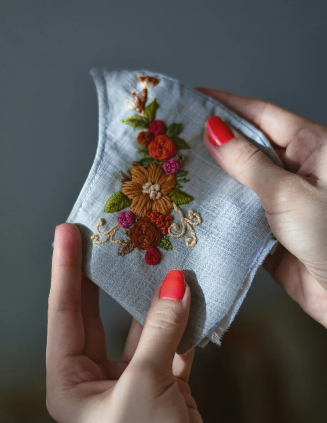 a woman's hands holding a piece of cloth with embroidered flowers on it