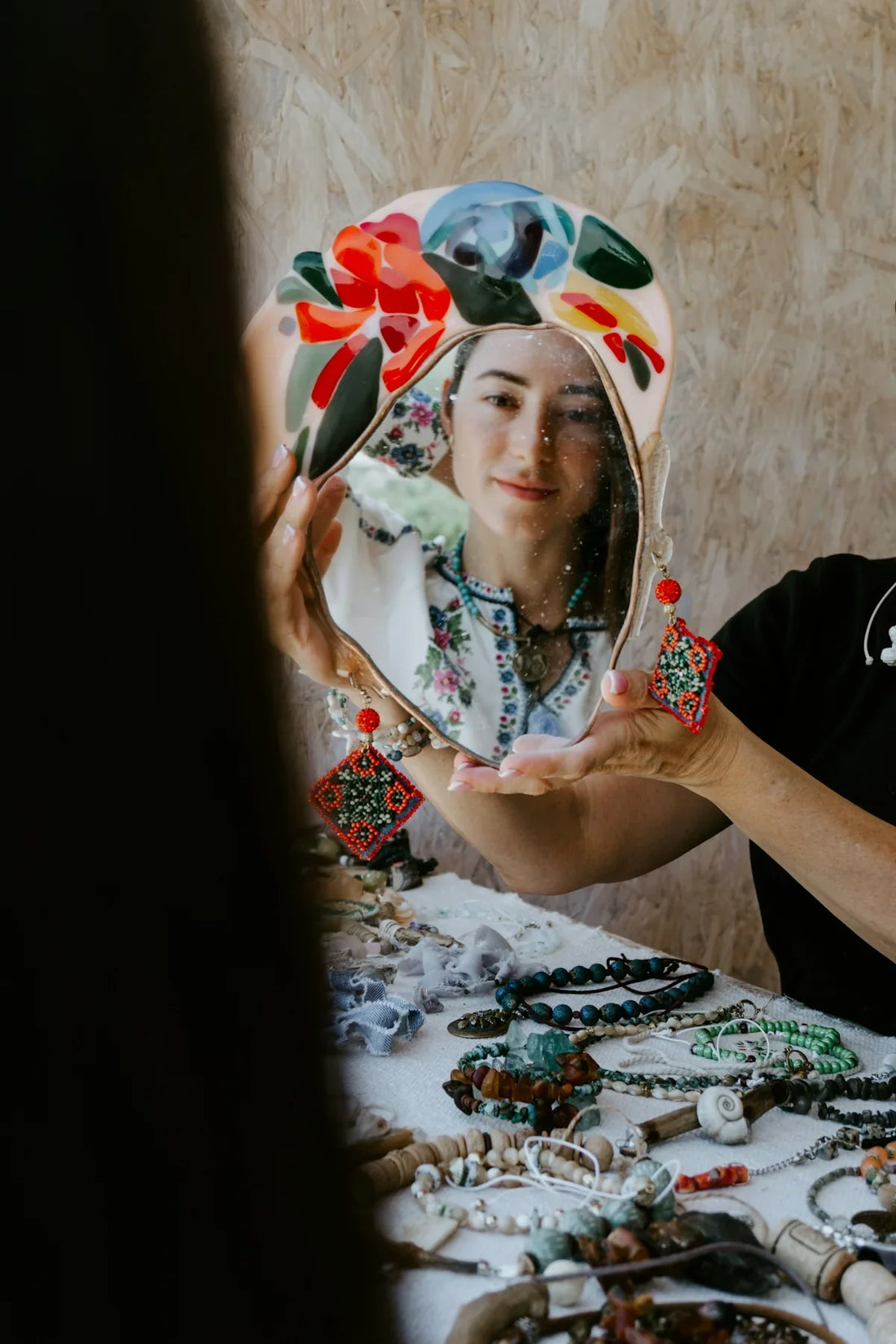 A woman holding a mirror over a table full of jewelry